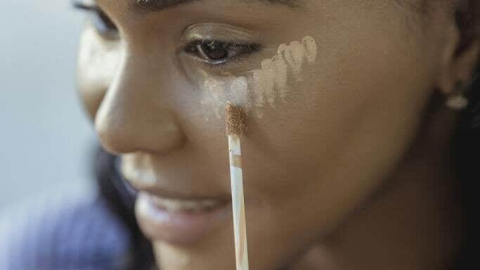 Crop black woman applying concealer on face