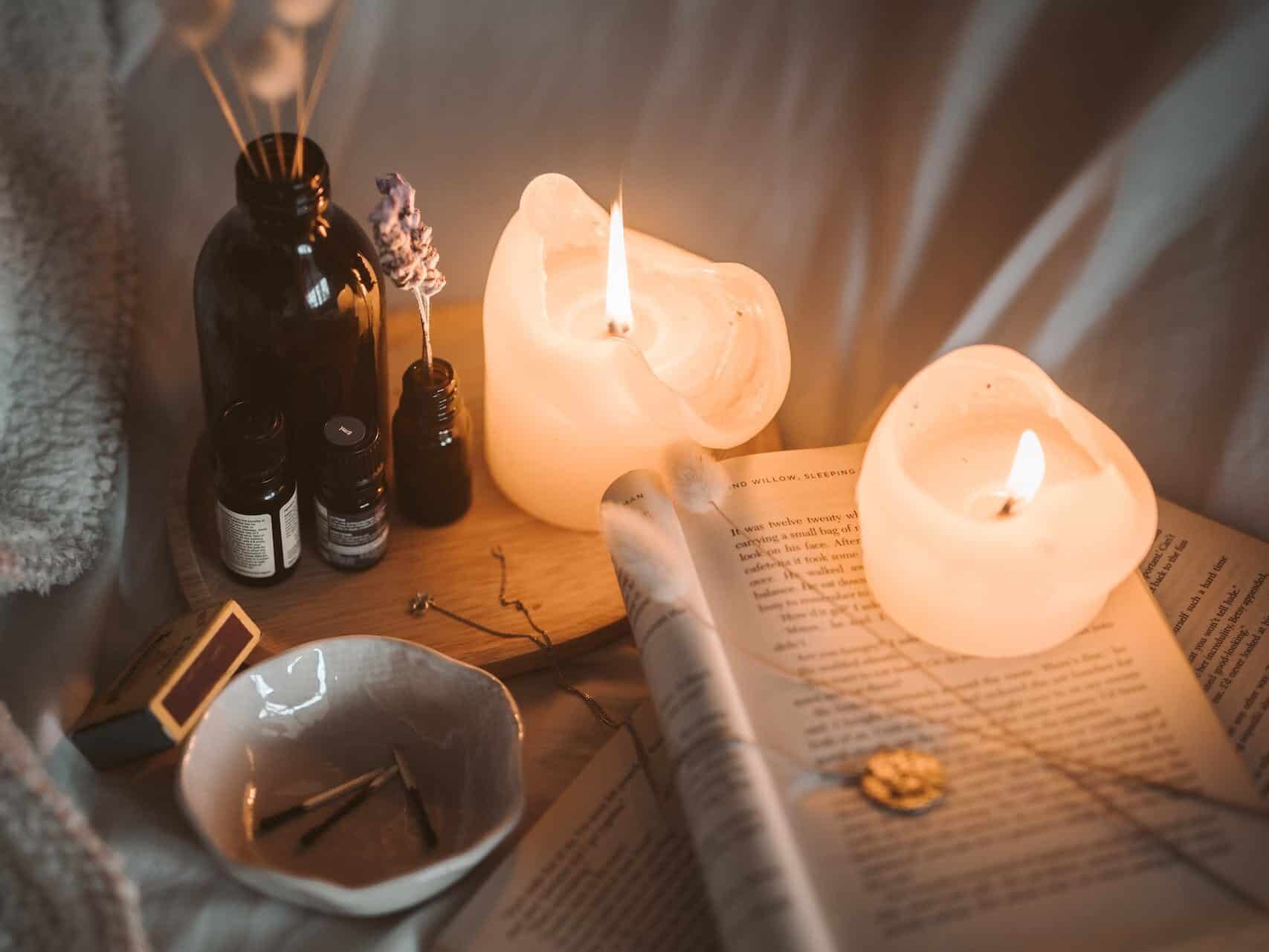 Lighted Candle on White Book Beside Black Glass Bottle