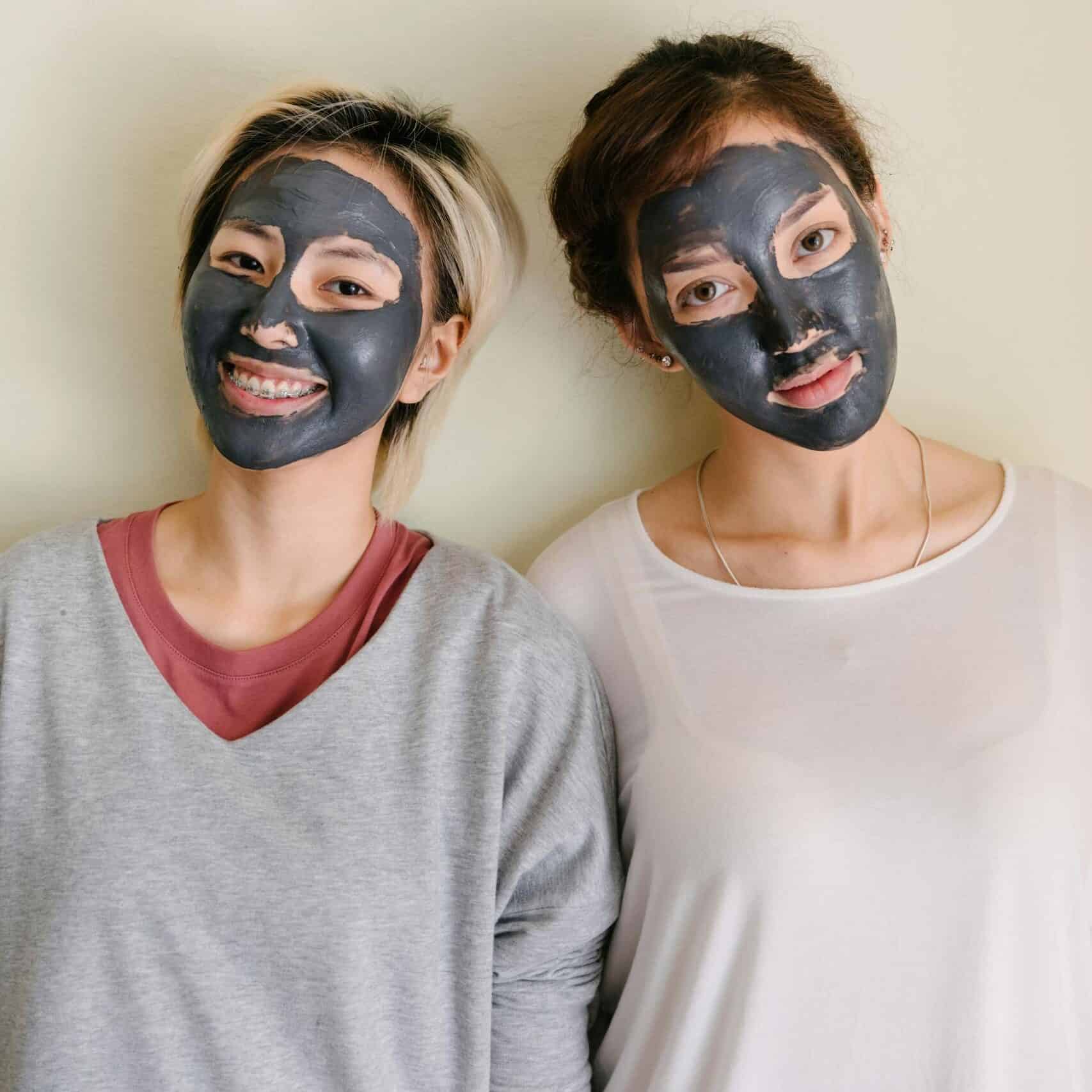 Young diverse women in casual clothes with black facial mud mask on beige background looking at camera charcoal mask